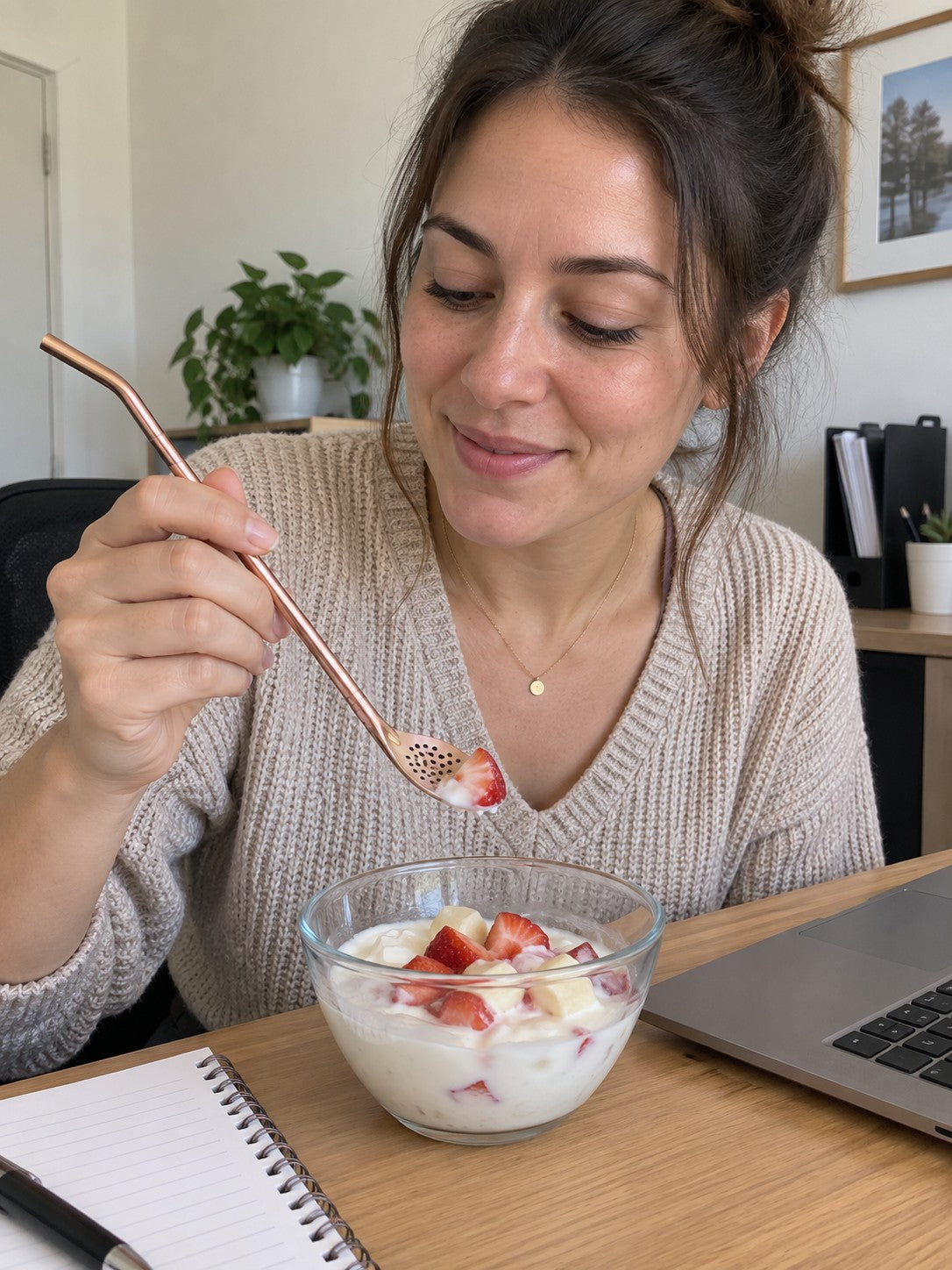 Woman using a rose gold spoon straw with strawberry yogurt at her desk