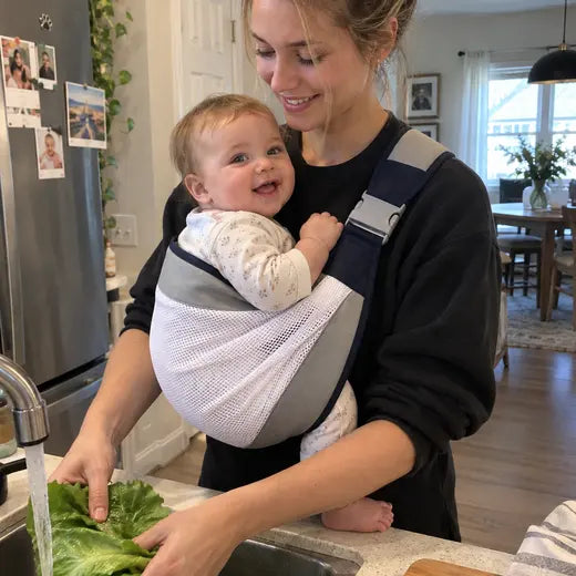 Mother wearing the sling carrier while rinsing lettuce in the kitchen