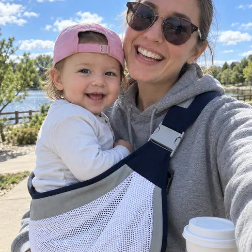 Mother wearing the mesh sling carrier outdoors while holding a coffee