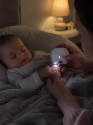 Parent trimming a sleeping baby's nails at night with LED light