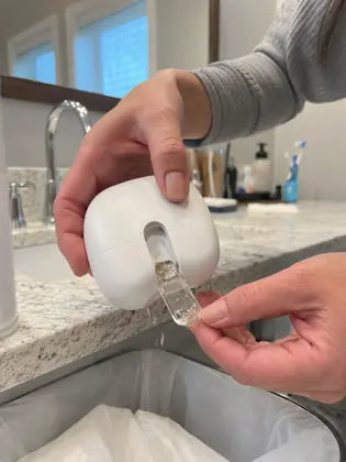 Electric nail clipper catcher being emptied over a bathroom trash bin