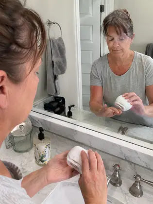 Woman using an electric nail clipper in front of a bathroom mirror