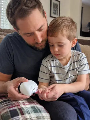 Father trimming a toddler's nails with an electric nail clipper at home