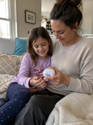Mother helping daughter trim nails with an electric nail clipper on a couch