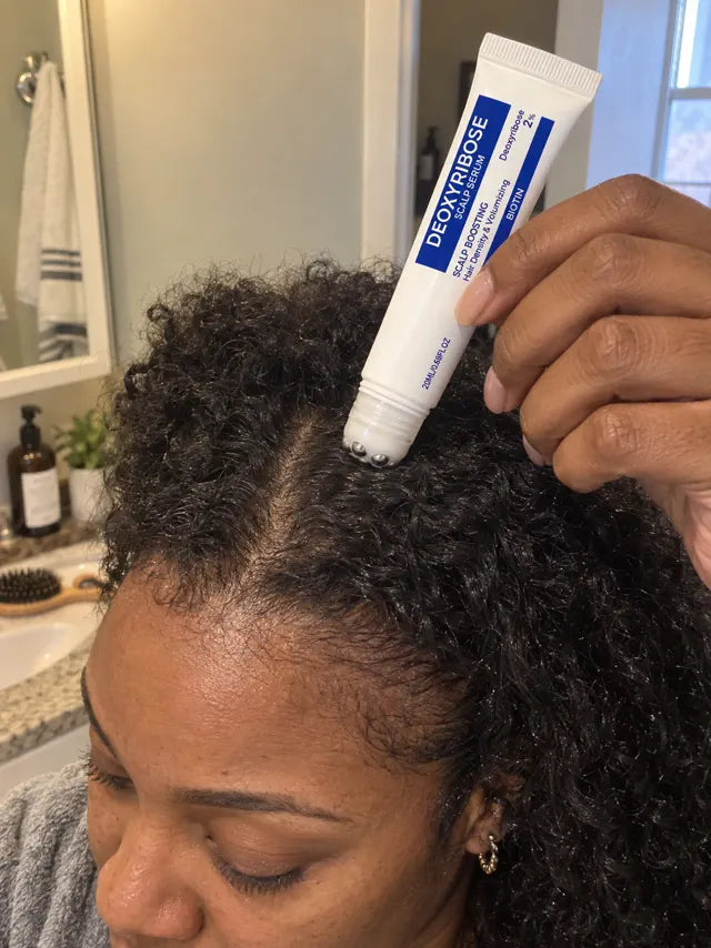 Woman applying scalp serum to curly hair at the part line