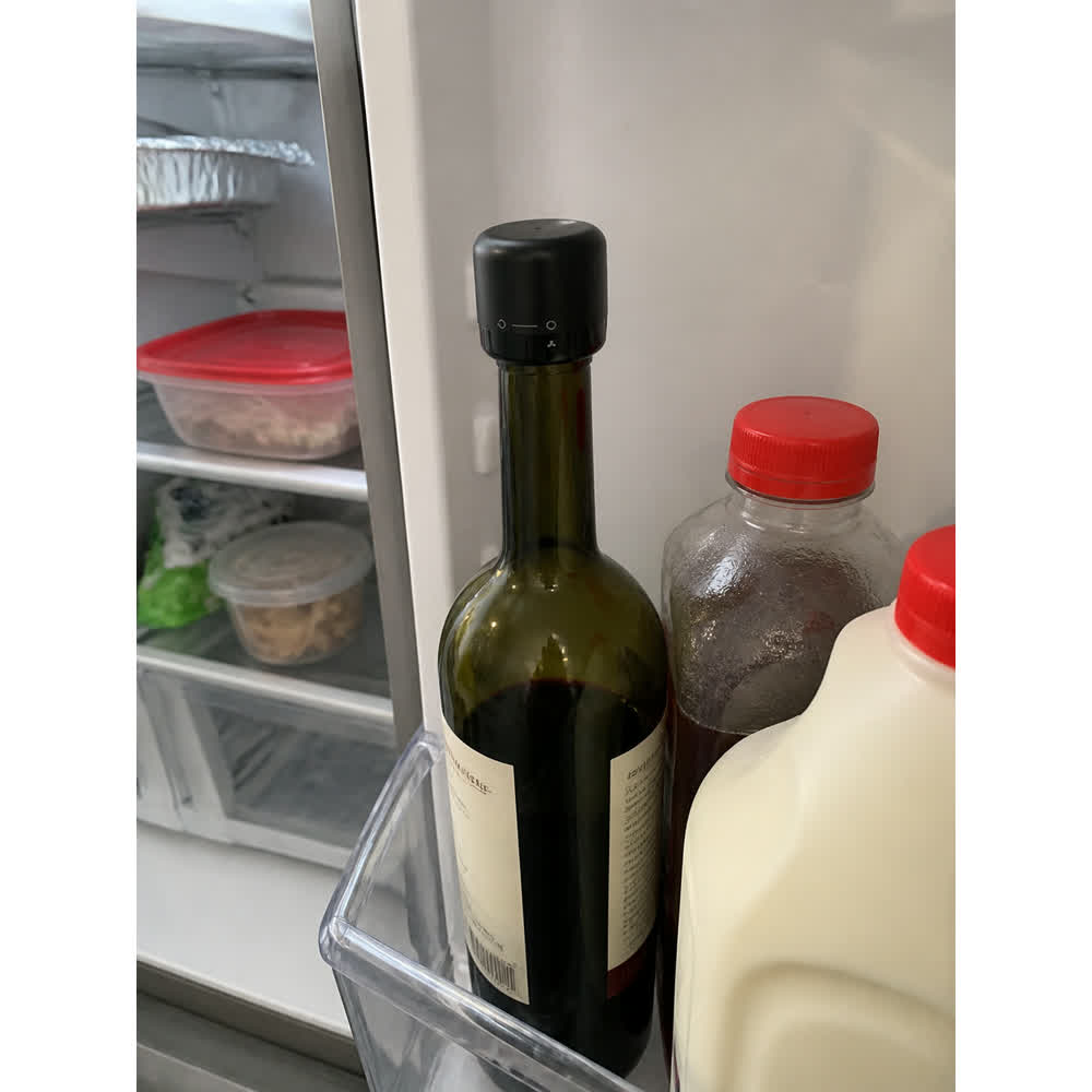 Regular wine bottle sealed with black stopper stored in a refrigerator door